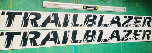 Two white vinyl decal stickers with the word 'Trailblazer' in black font, placed against a background with measurements for cutting.